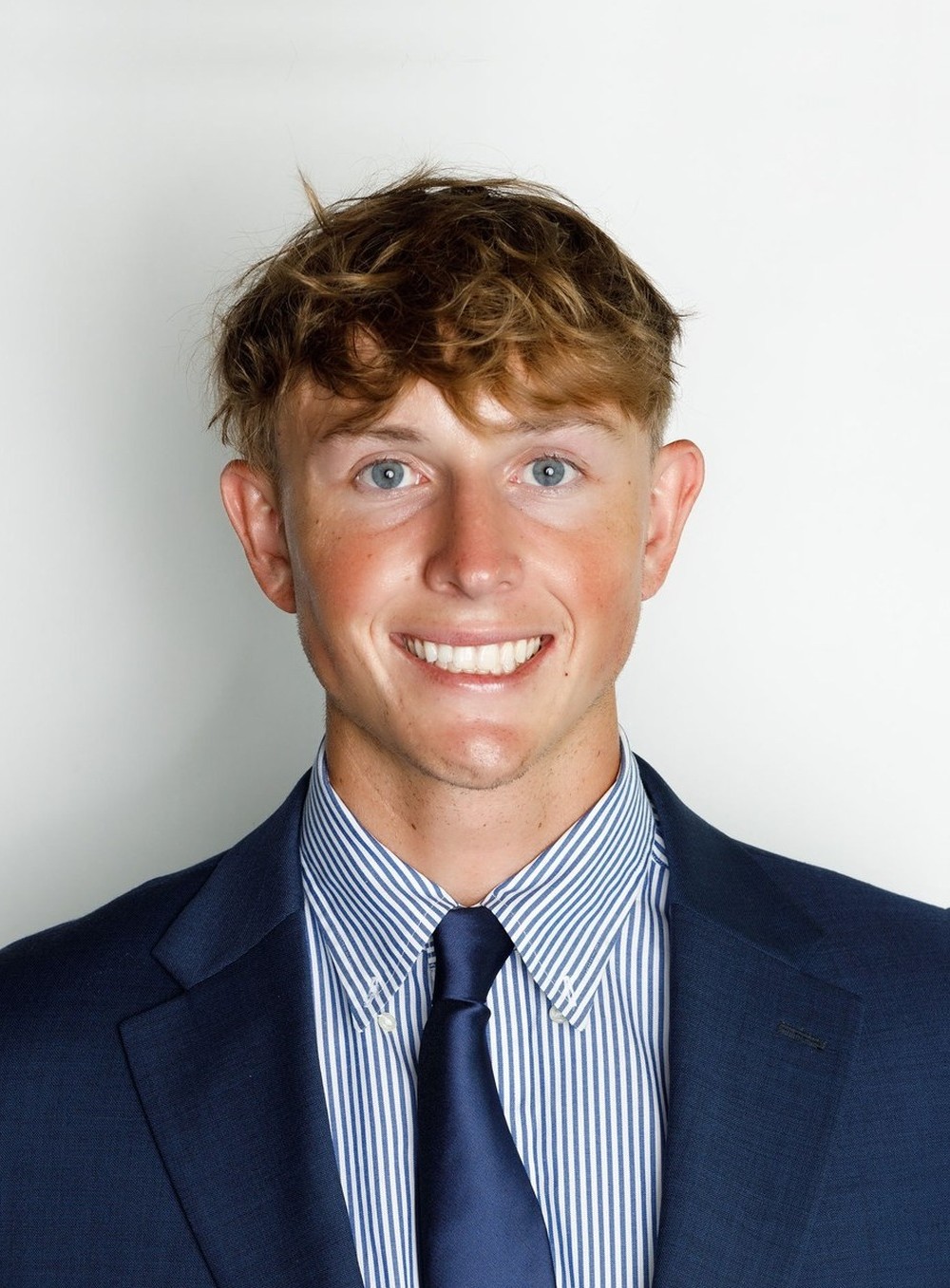 Zach Wadas studio headshot — navy suit and tie, smiling